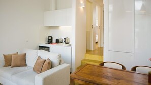 A compact living space with a kitchenette, a sofa with cushions, a wooden dining table, and a staircase leading to another room. - Graça Hidden Garden by LovelyStay 5 (Lisboa)