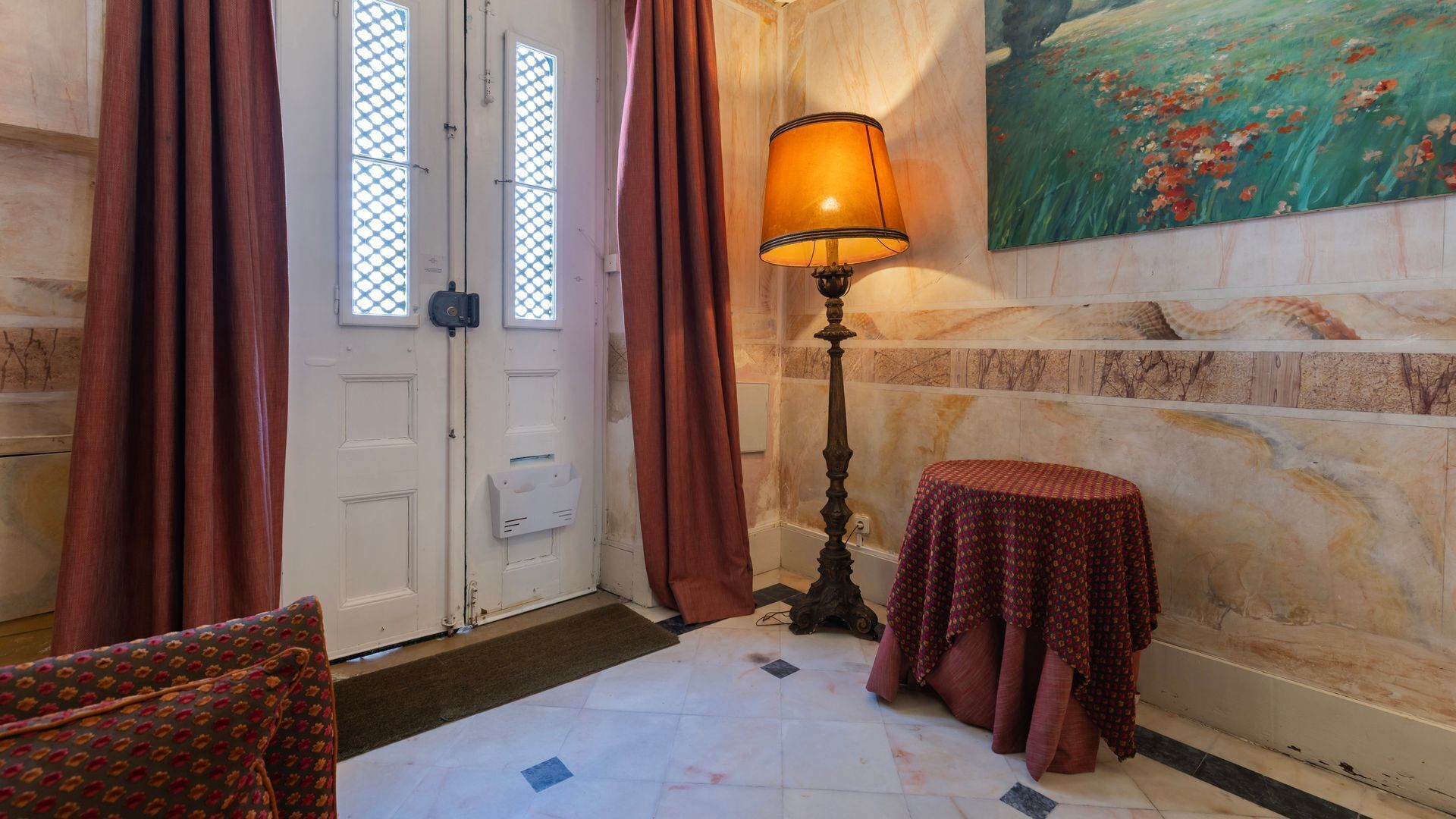 A room with a door, a lamp, a small table, and a painting on the wall.