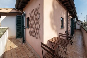 A balcony with a wooden table and chairs, a lattice wall, and a building with a sloped roof. - Stunning Rooftop Views in the Heart of Trastevere (Roma)