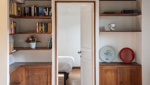 Ein Zimmer mit einem Bett, Holzregalen mit Büchern, einer weißen Tür und einem Schrank mit zwei Tellern.
