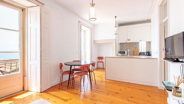 Une cuisine moderne avec un coin repas, un plancher en bois et une vue sur l’extérieur grâce à la porte ouverte.