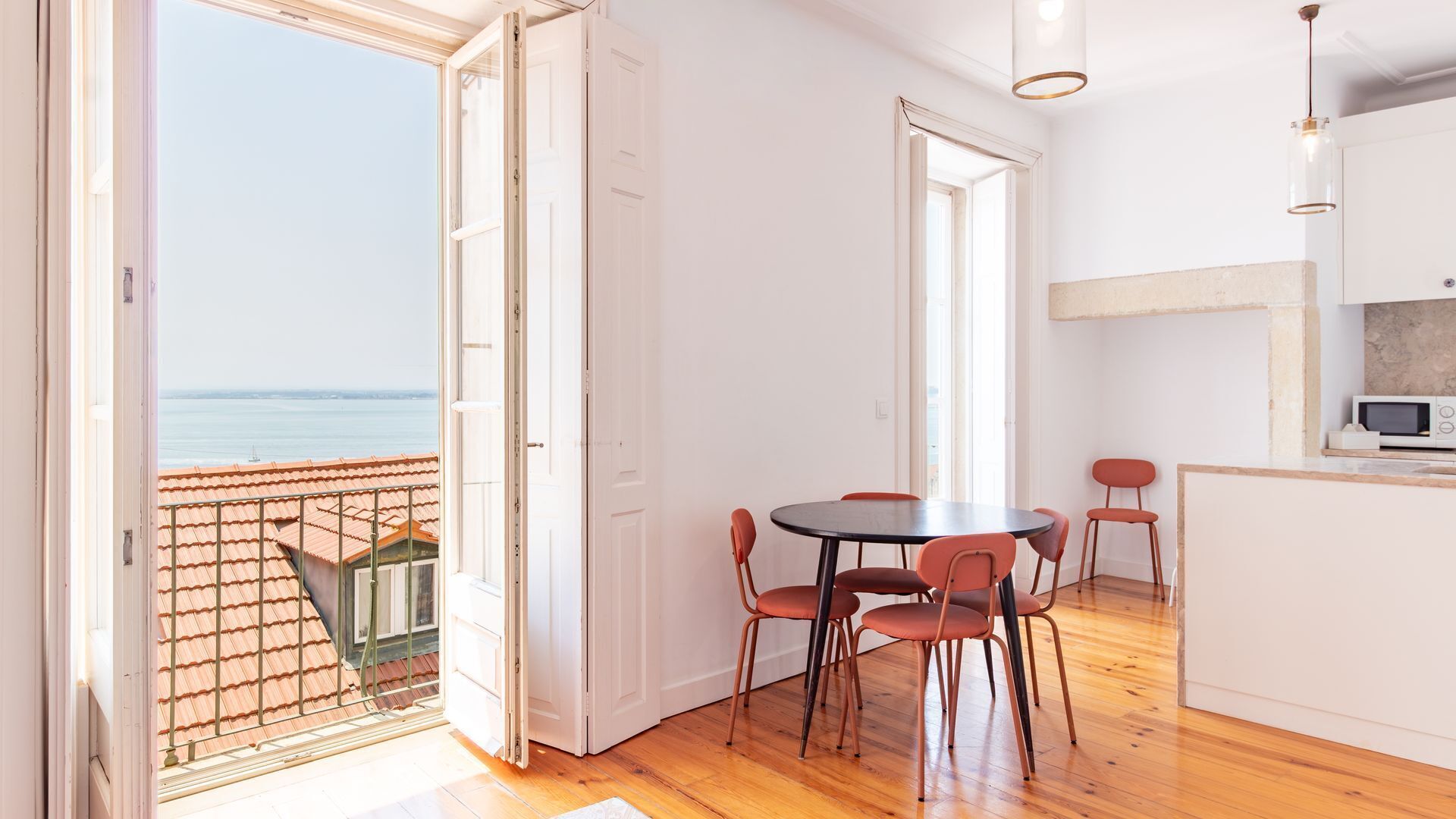Una habitación con balcón, un comedor con sillas y una zona de cocina con microondas.