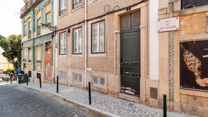 Une rue bordée d’un immeuble dont la façade présente un motif décoratif et sur lequel on peut lire l’inscription « Rua de São Mamede ».