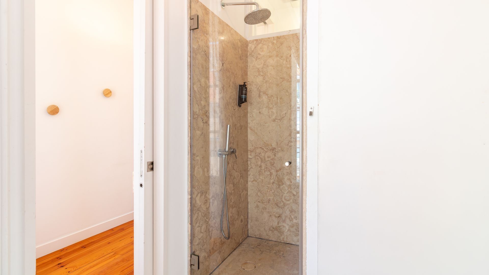 Un baño con ducha, paredes de mármol y suelo de madera.