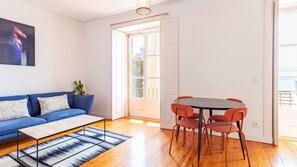 A modern living room with a blue sofa, a coffee table, and a dining table with chairs. - Alfama Balcony River View by LovelyStay (Lisboa)