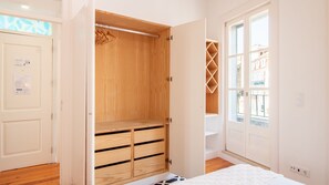 Een slaapkamer met een houten garderobe, een bed en een raam met uitzicht op gebouwen.