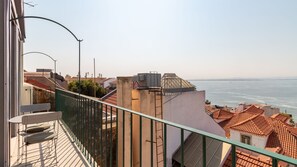Een balkon met uitzicht op zee, een lantaarnpaal en een gebouw met een pannendak.
