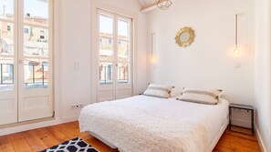 Ein Schlafzimmer mit einem großen Bett, Blick auf Gebäude durch das Fenster und einer Wandleuchte.