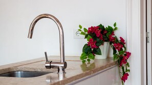 A kitchen sink with a modern faucet, a marble countertop, and a potted plant with red flowers. - Alfama Terrace River View by LovelyStay (Lisboa)