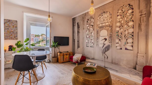 A modern living room with a large window, a dining area, and a decorative wall with intricate patterns. - Charm and Comfort 1BR Apartment in Principe Real (Lisbon)