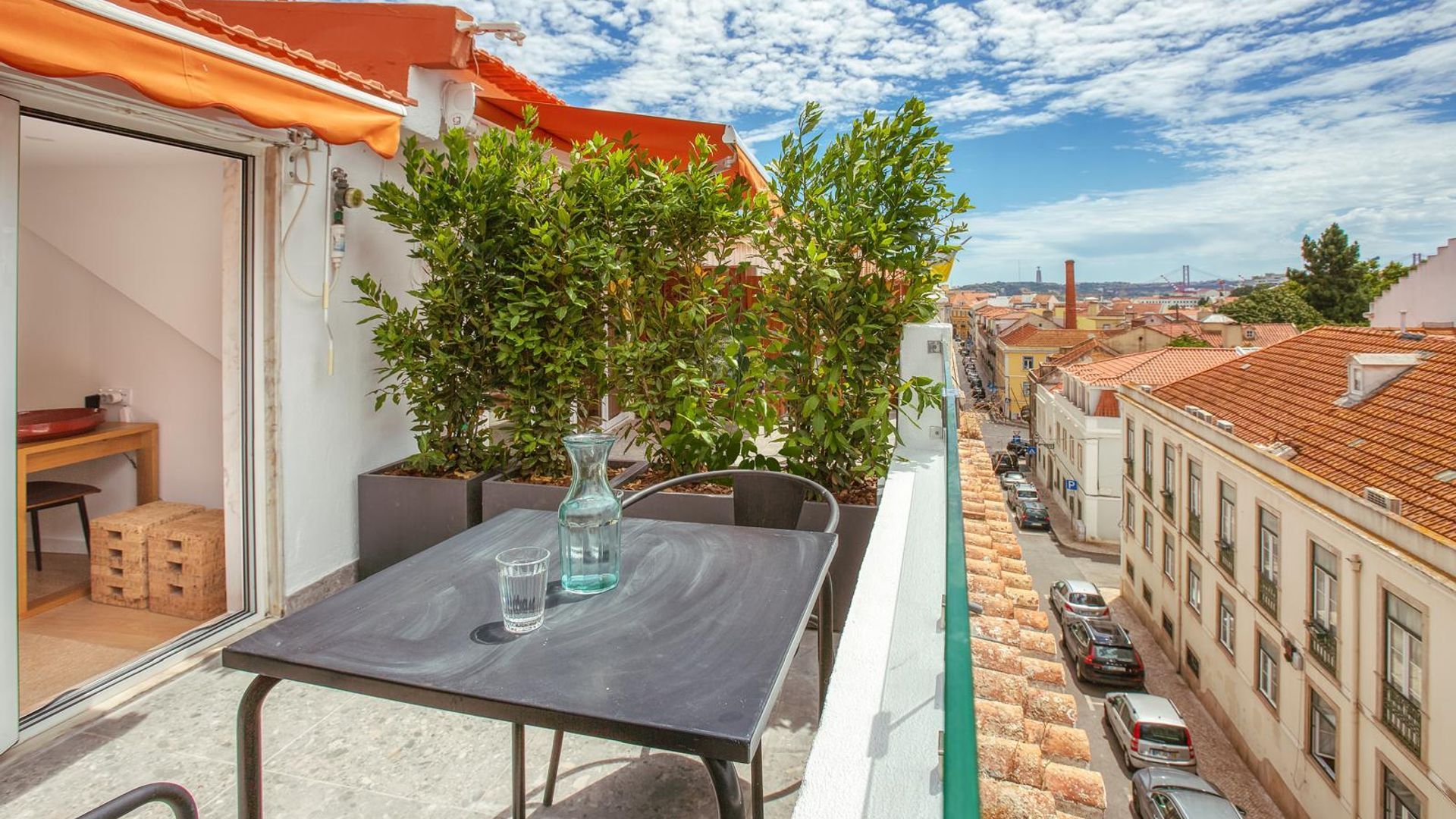 A balcony with a table, chairs, a potted plant, and a view of the cityscape.