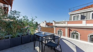 Terraço com mesa e cadeiras, rodeado por plantas em vasos.
