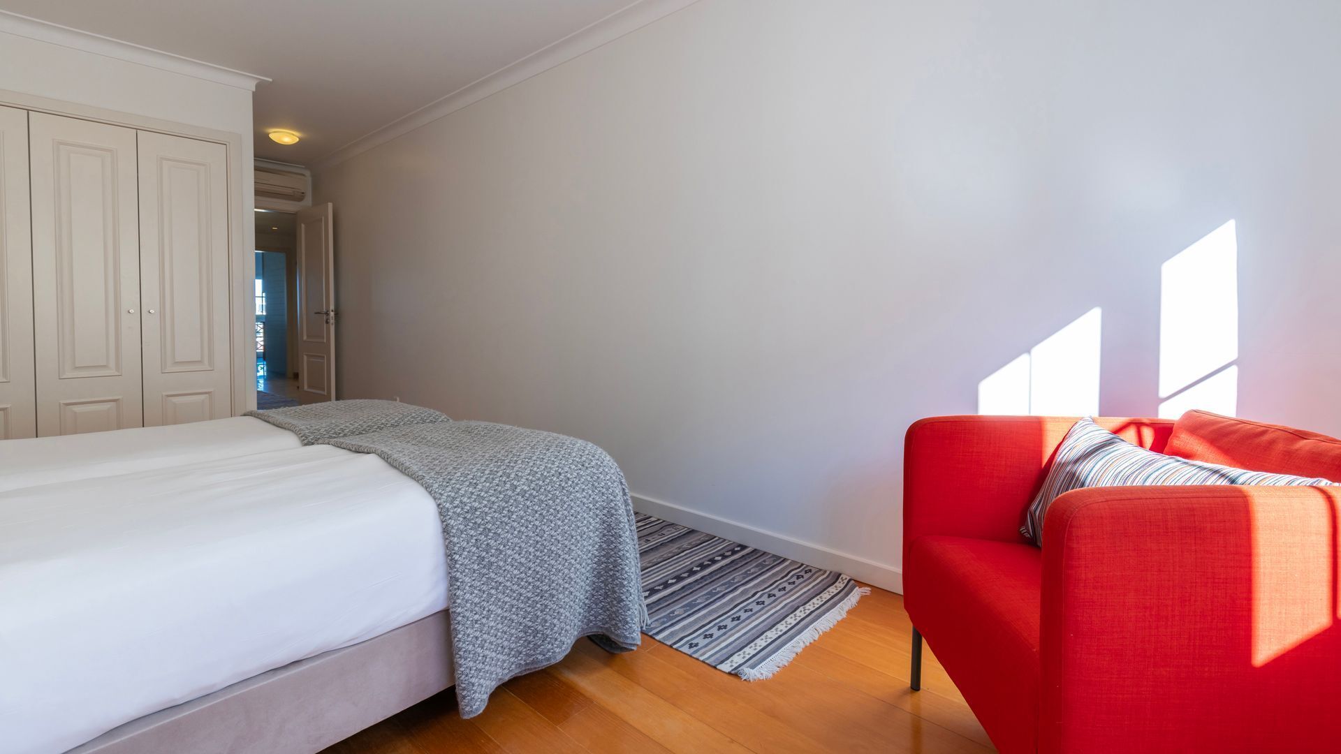 A bedroom with a bed, a red sofa, a patterned rug, and a white wardrobe.