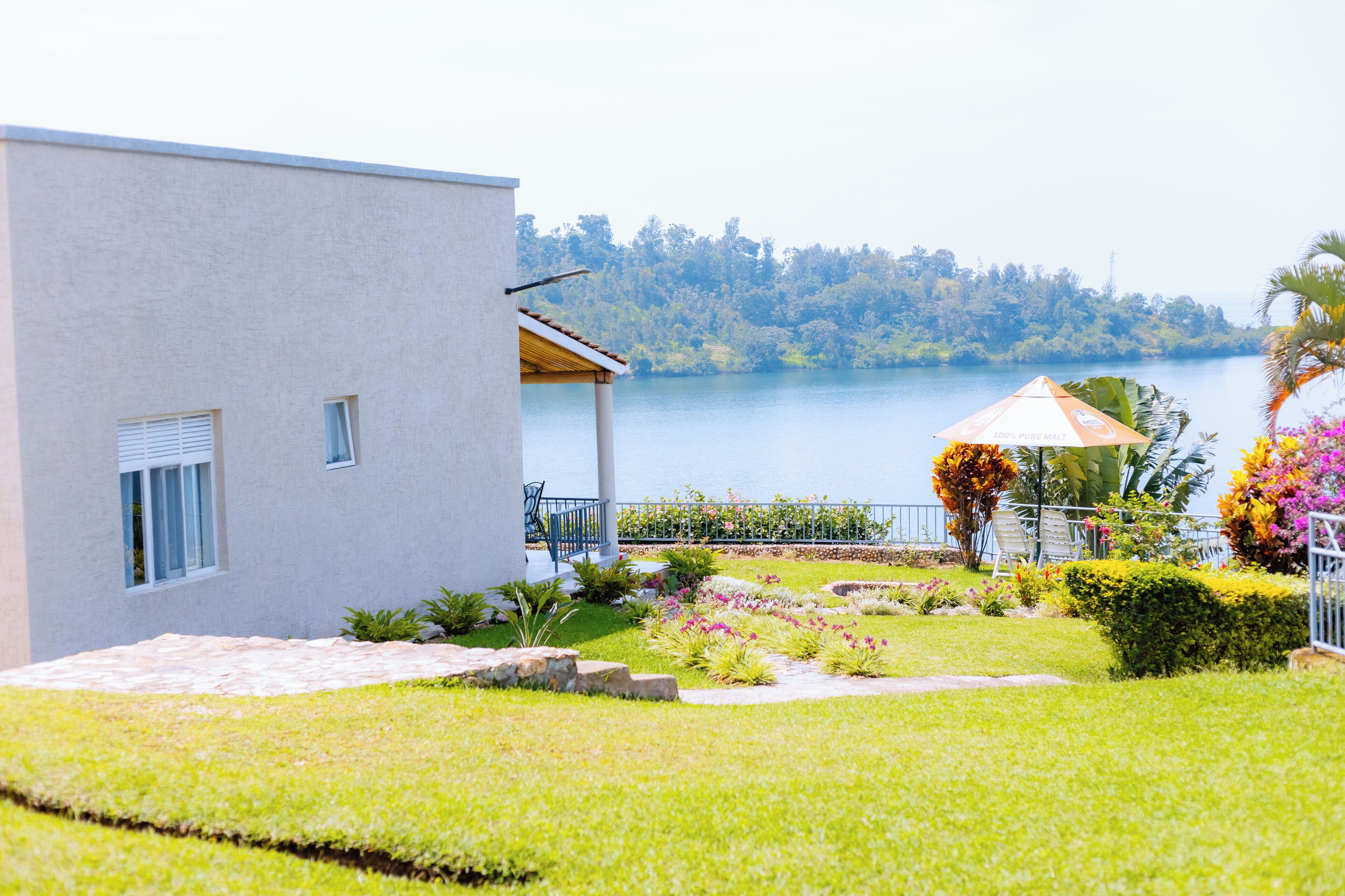 A modern building with a balcony overlooking a lake, surrounded by well-maintained gardens and a patio area.