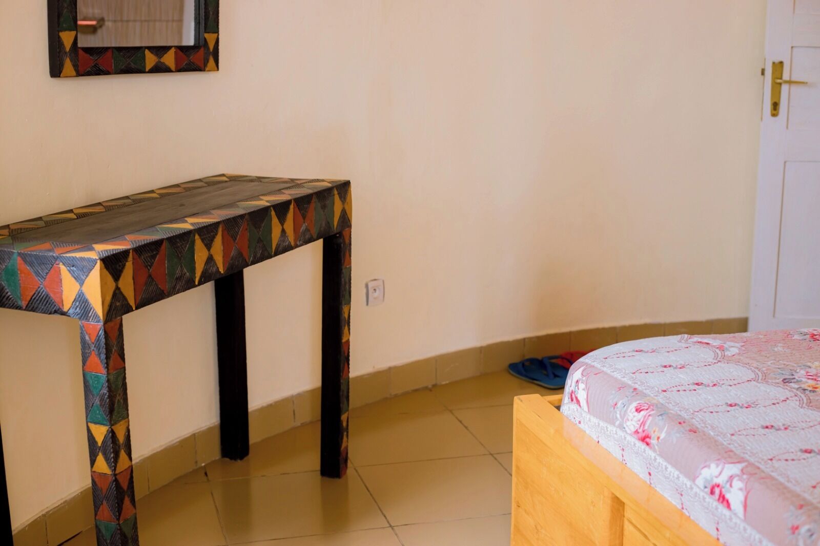 Una habitación con una cama, una mesita pequeña y un espejo fijado a la pared.