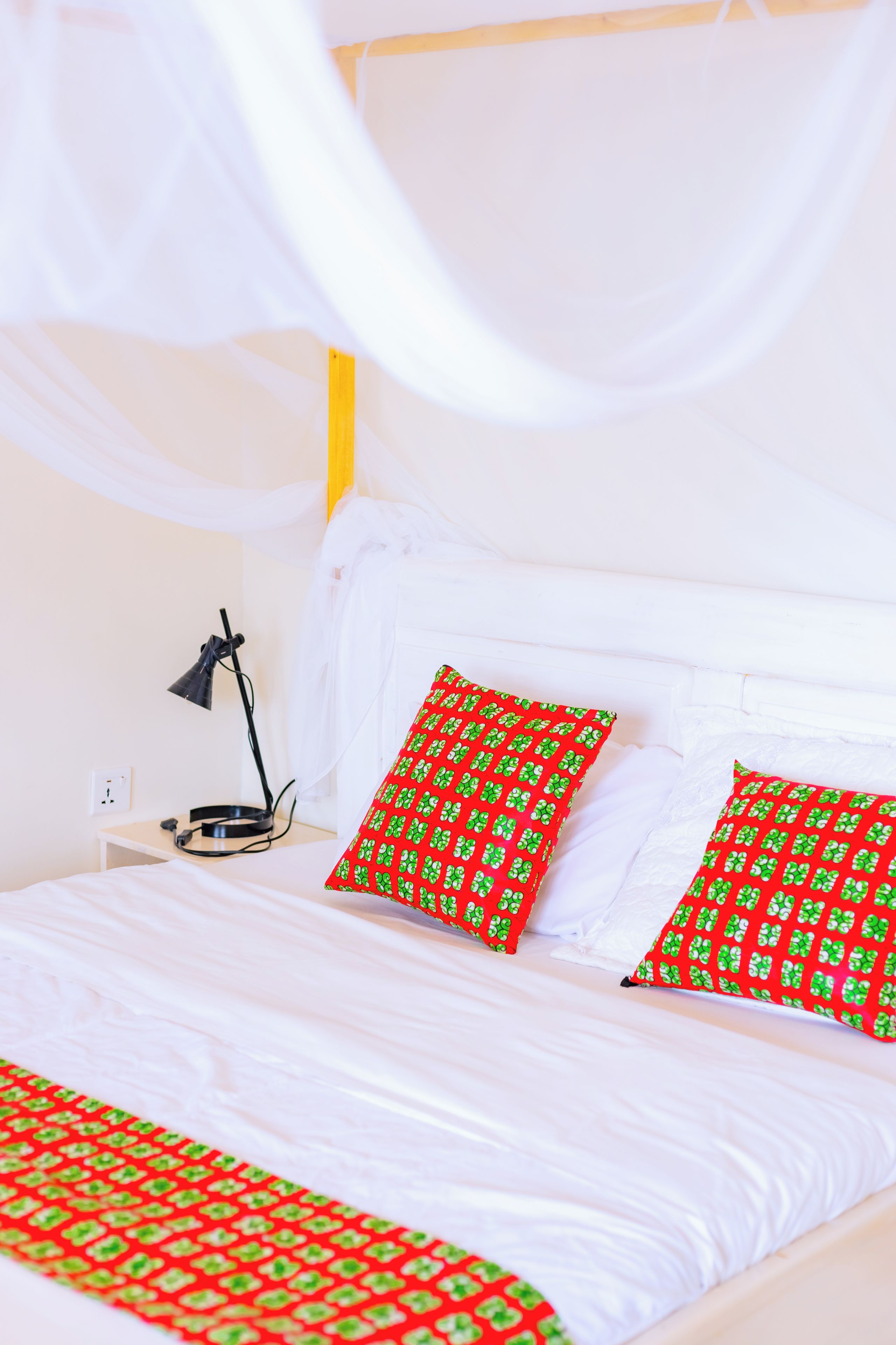 Een bed met witte lakens en twee kussens met een rood en groen patroon.