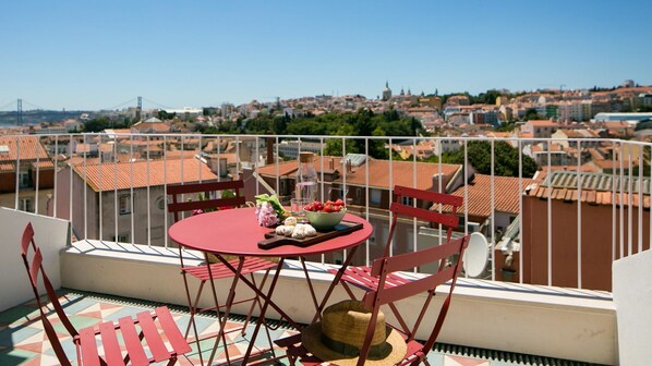 A balcony with a red table and chairs, a bowl of strawberries, and a bottle of water. - Central Rooftop Apartment by LovelyStay (Lisbon)