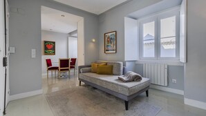 Ein modernes Wohnzimmer mit einem grauen Sofa, einem kleinen Tisch und roten Stühlen. Ein Fenster bietet Blick auf einen Berg.