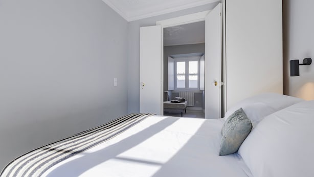 Ein Schlafzimmer mit einem Bett, einem Nachttisch, einem Stuhl und einem Fenster.