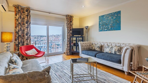 Ein Wohnzimmer mit einer Couch, einem roten Sessel und Blick auf die Stadt vom Balkon aus.