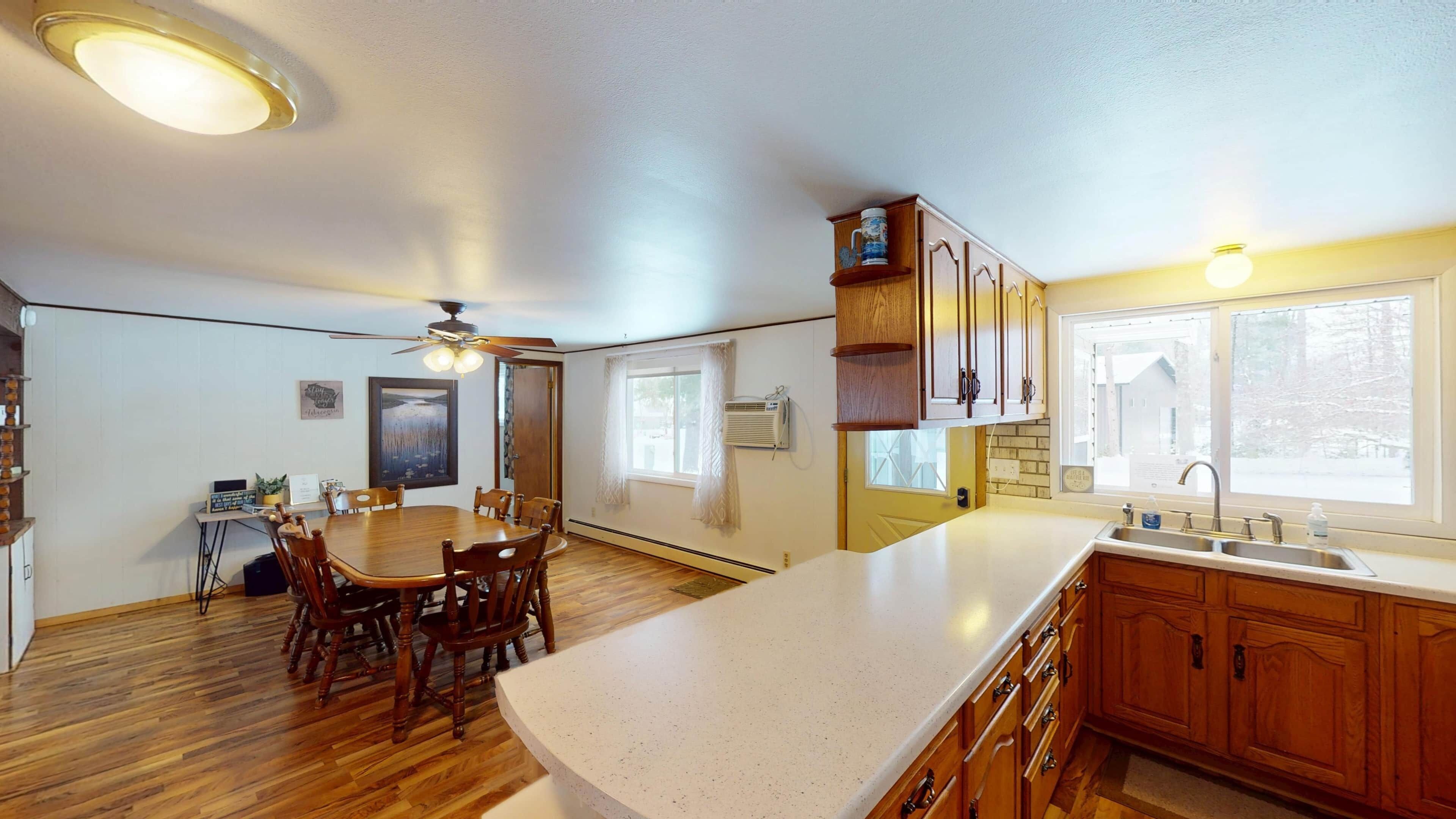 A kitchen with wooden cabinets, a white countertop, a dining table with chairs, and a ceiling fan.