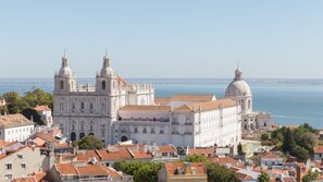A historic white building with multiple domes and towers, surrounded by red-tiled roofs and greenery, overlooking a body of water. - Penthouse Terrace 360º Lisbon View by LovelyStay (Lisboa)