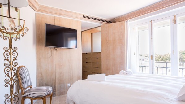 A hotel room with a bed, a TV mounted on the wall, a chair, and a large window offering a view of the outdoors. - Penthouse Terrace 360º Lisbon View by LovelyStay (Lisboa)