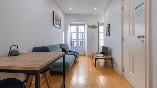 Een moderne woonkamer met een houten eettafel, een bank, een televisie en een openslaande balkondeur.