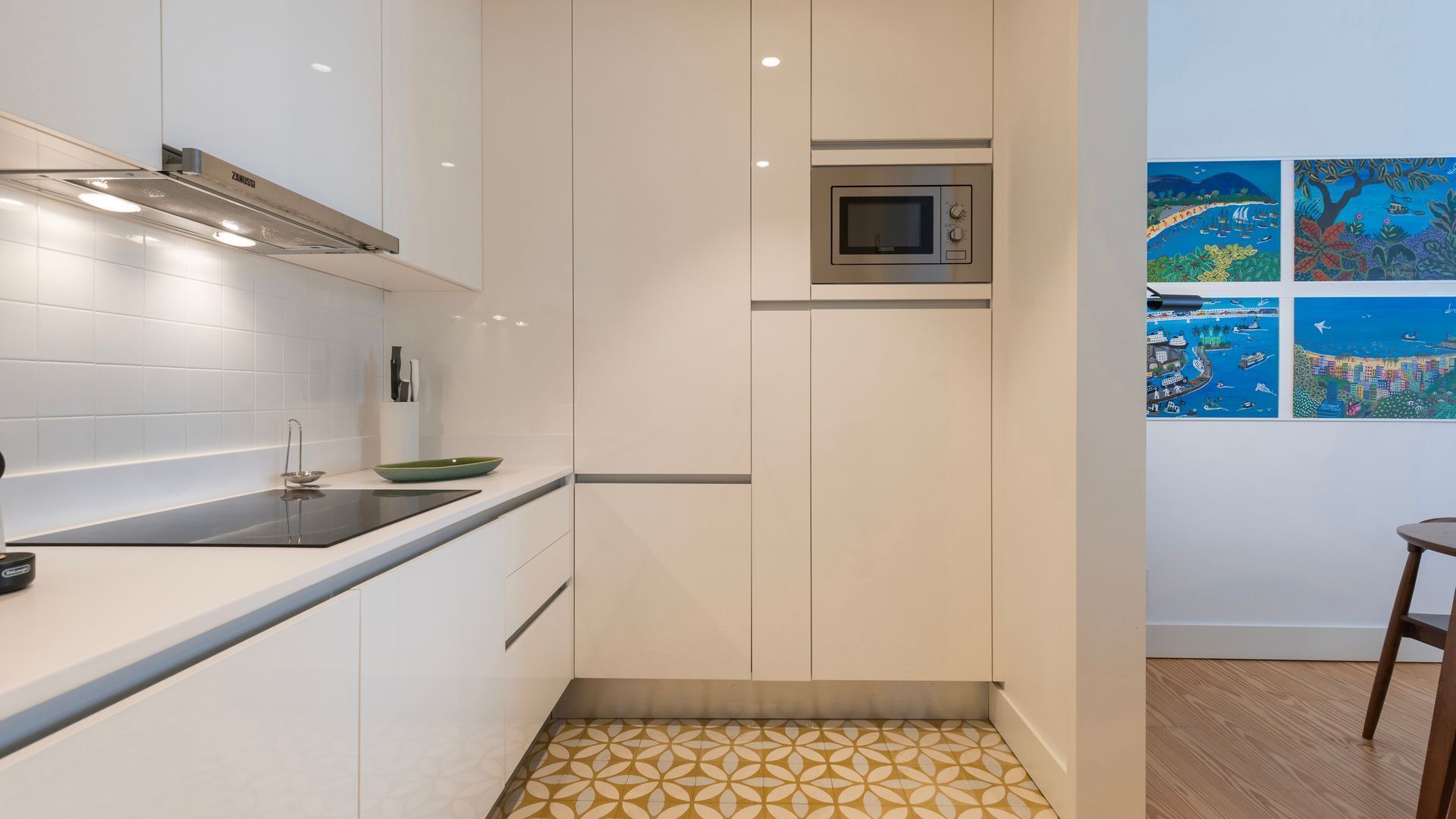 Een moderne keuken met witte kasten, een zwart inductiekookveld, een magnetron en een klein eiland met een groene kom.