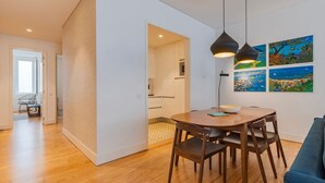Ett modernt matområde med ett träbord och stolar, en blå soffa och ett kök som syns genom en öppen dörr.