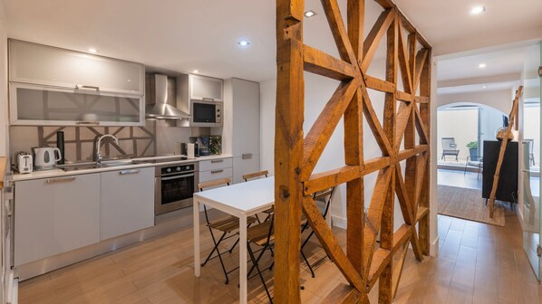A modern kitchen with stainless steel appliances, a dining area with a wooden table, and a view of the living area through a wooden partition. - 1BDR w/ Terrace in Alfama Centre by LovelyStay (Lisboa)