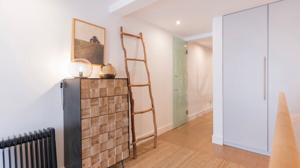 Un pasillo con un radiador, un armario de madera, una escalera, un cuadro enmarcado y un guardarropa.