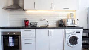 Une cuisine compacte équipée d’un four encastré, d’une machine à café, d’un grille-pain et d’un lave-linge.