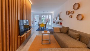 Ein modernes Wohnzimmer mit Fernseher, Wandverkleidung aus Holz, einer Couch und einem Essbereich mit Stühlen und Tisch.