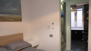 A bedroom with a bed, a white bedside table, a nightstand, a wall-mounted light fixture, and a door leading to a bathroom. - Just minutes away from San Siro and San Carlo Hospital. (Milano)