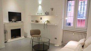 A living room with a fireplace, a television, a round glass table, a beige armchair, and a sofa. - Just minutes away from San Siro and San Carlo Hospital. (Milano)