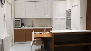 A compact kitchen with white cabinets, a microwave, and a built-in oven. There is a small dining area with a table and chairs. - Just minutes away from San Siro and San Carlo Hospital. (Milano)