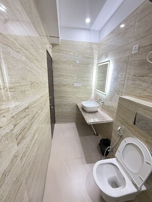 A modern bathroom with a marble wall, a sink, a mirror, and a toilet. - HOTEL CROWN PLAZA (Prayagraj)