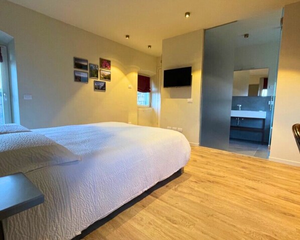 Une chambre dotée d’un grand lit, d’un téléviseur à écran plat fixé au mur et d’une salle de bain visible à travers une porte ouverte.