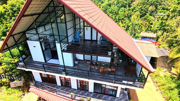 A two-story building with a large glass facade, a red roof, and a balcony with seating. - Ella Mountain Breeze Villa: King Suite with Balcony (Ella)