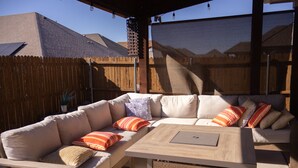 Een terras met een houten tafel en beklede banken, een houten omheining en een heldere lucht.