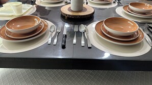 Een eettafel gedekt met diverse kommen en bestek, een potplant en een koffiezetapparaat op de achtergrond.