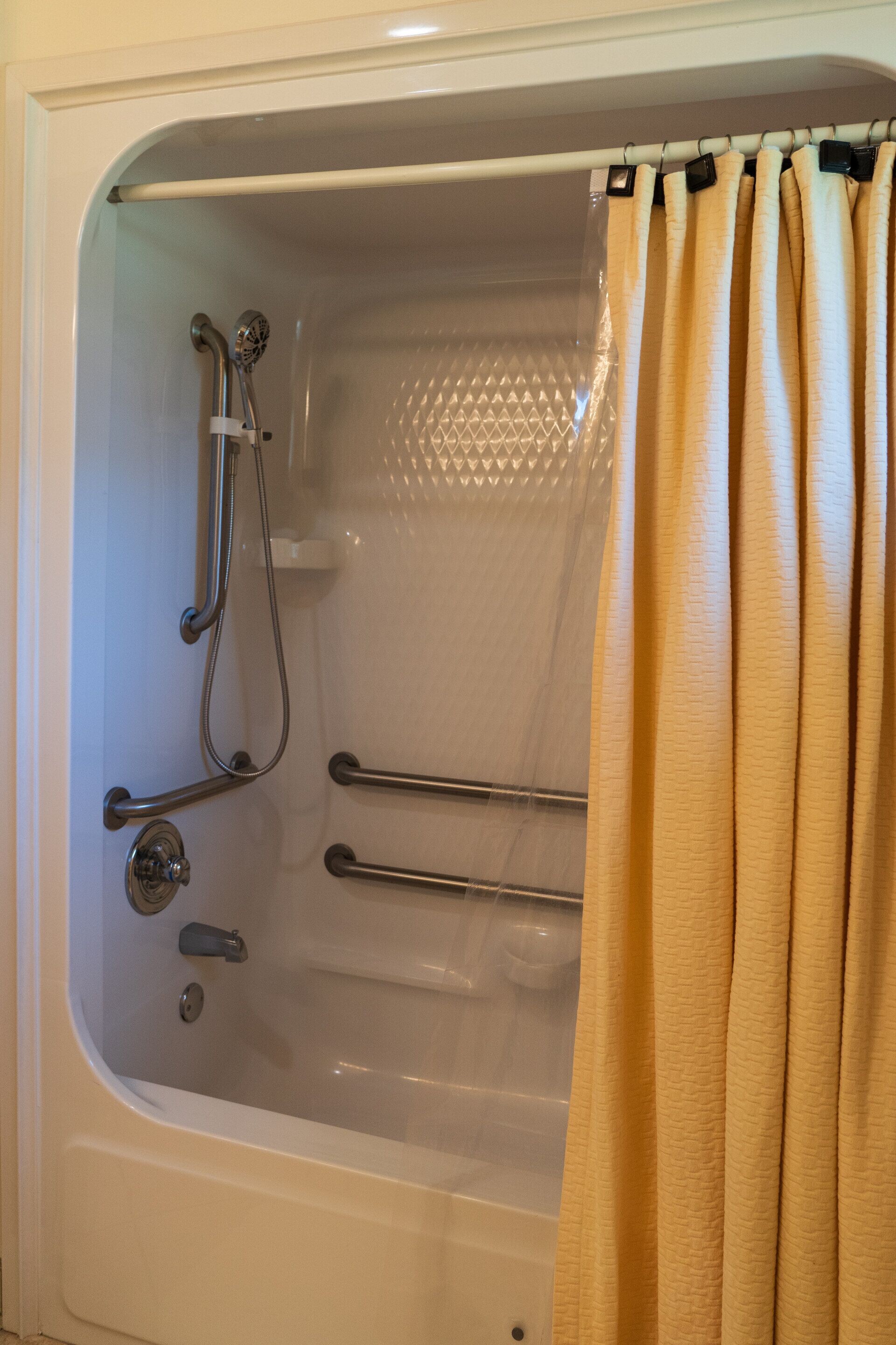 A bathtub with a showerhead, grab bars, and a curtain.
