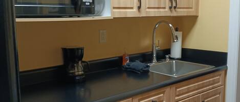 A kitchen with wooden cabinets, a microwave, a sink, and a coffee maker.