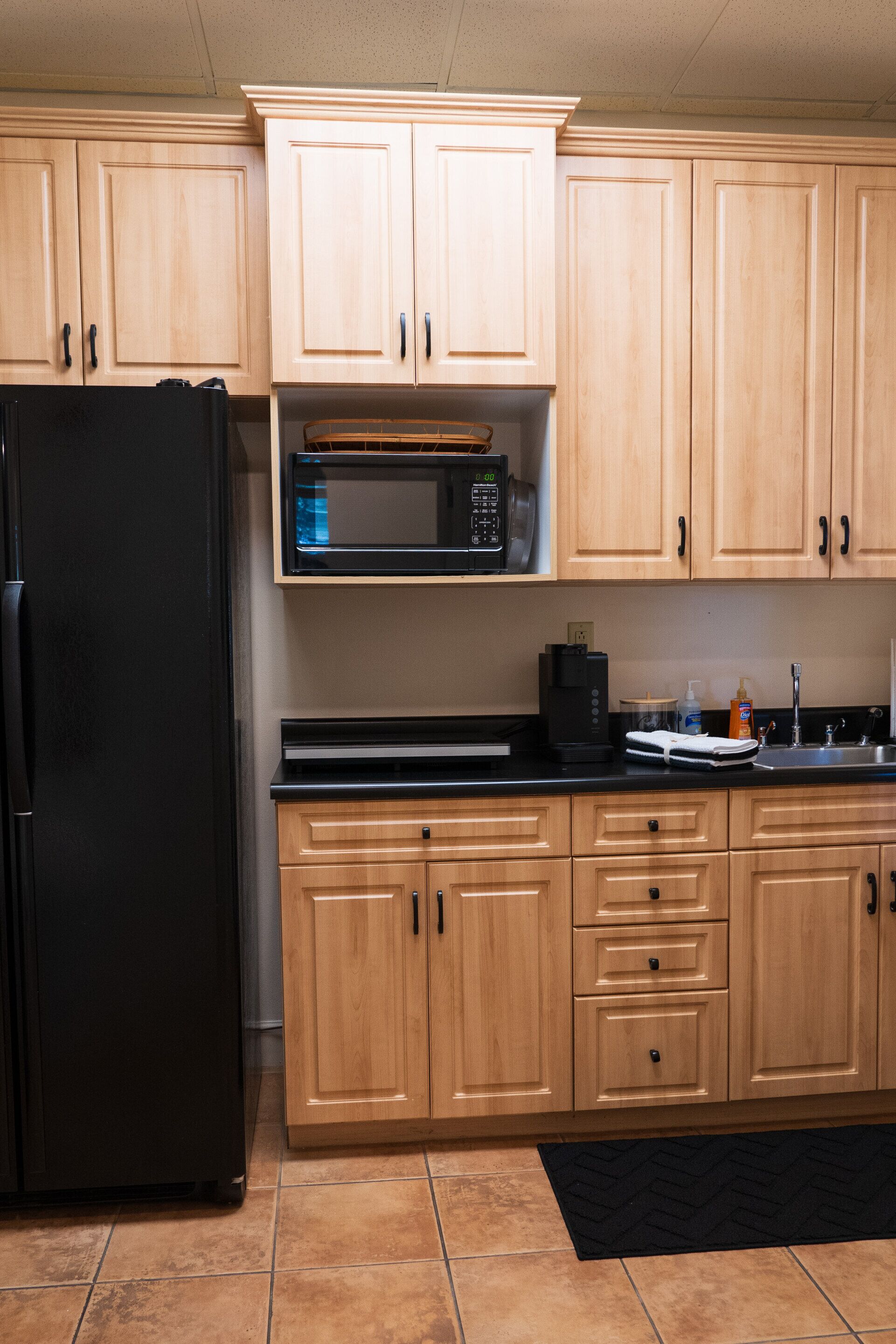 Una cocina con armarios de madera, un refrigerador negro, un microondas y un lavamanos.