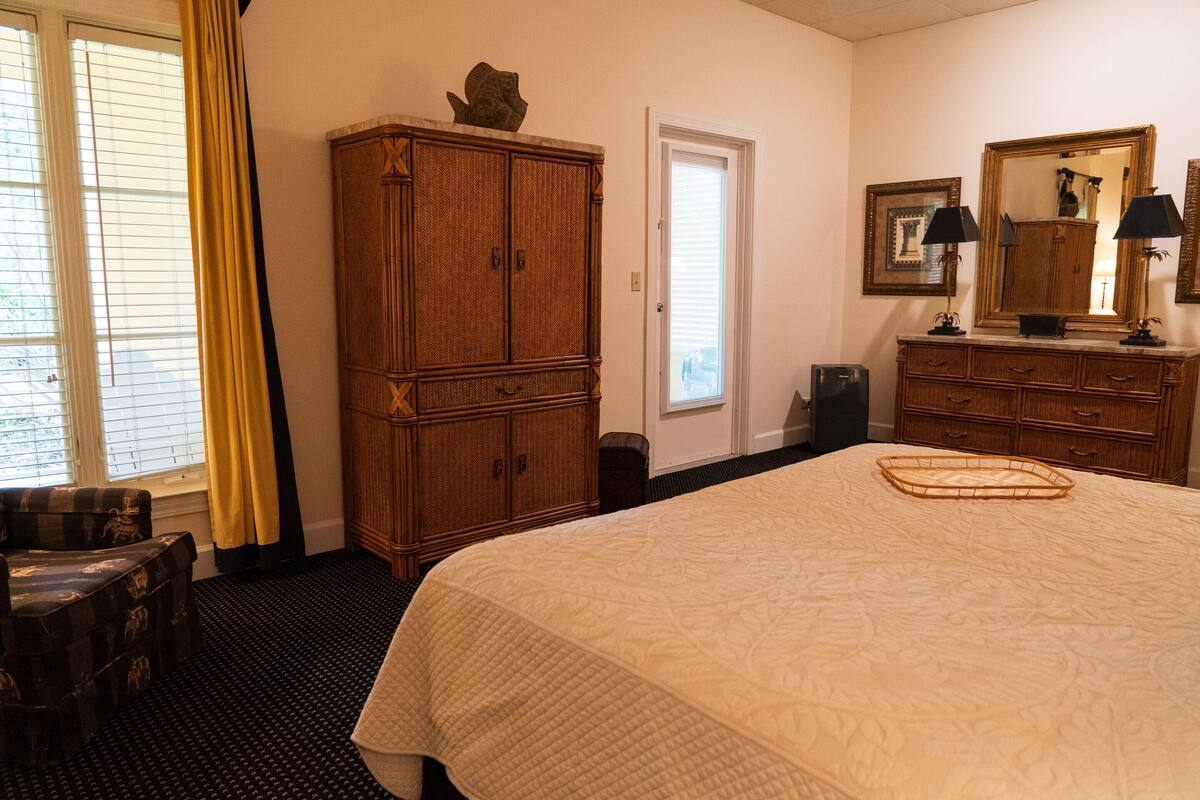 Camera d'albergo con un letto grande, un armadio in legno, una poltrona, uno specchio e una finestra con tende.