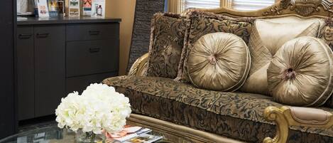 A living room with a patterned sofa, a glass coffee table, and a bookshelf with various items.