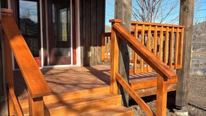 Un escalier en bois mène à un porche couvert doté d’une porte d’entrée en verre.