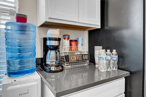 Un comptoir de cuisine équipé d’un distributeur d’eau, d’une machine à café et d’un espace dédié au café, avec des bouteilles et des récipients d’eau.