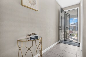 Un couloir avec une porte vitrée donnant sur l’extérieur, une petite table avec des livres et un tableau encadré au mur.